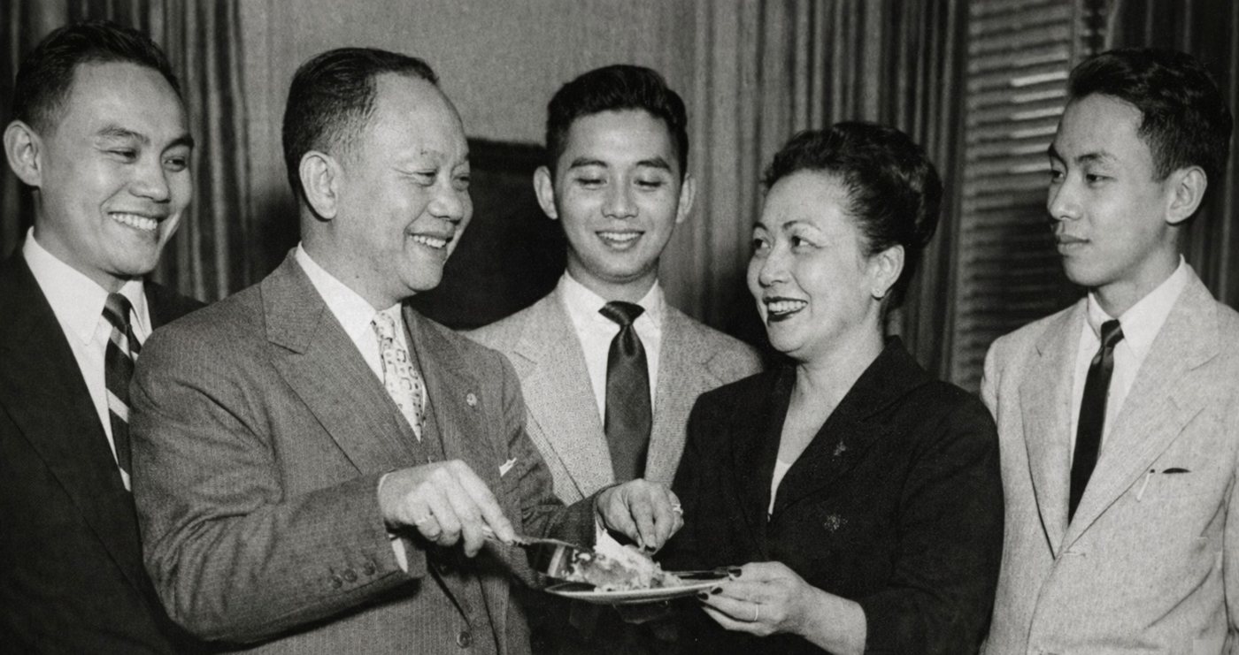 Club President Charlie Romulo, smiling, cutting a birthday cake with members in 1936