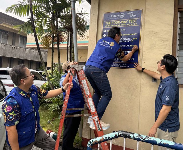 Rotarians steady a ladder as a member mounts the Four-Way Test marker at Hospicio de San Jose, at the Project R.I.V.E.R. turnover in December 2025