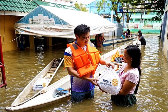 President Reginald Yu hands relief goods to a resident of Barangay Bulusan, where floodwater still surrounded homes.